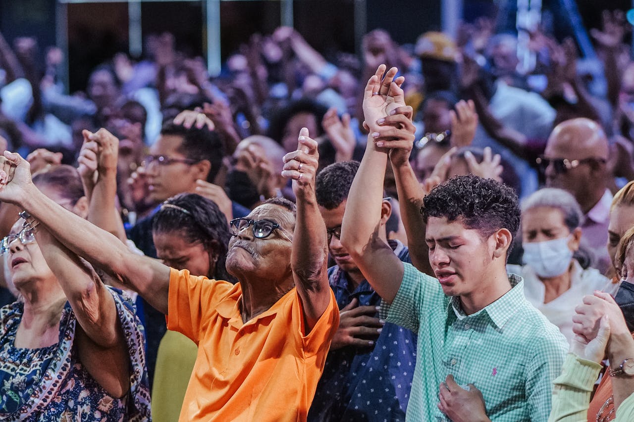 A diverse crowd engaged in a communal act of worship, raising hands in unity and prayer.