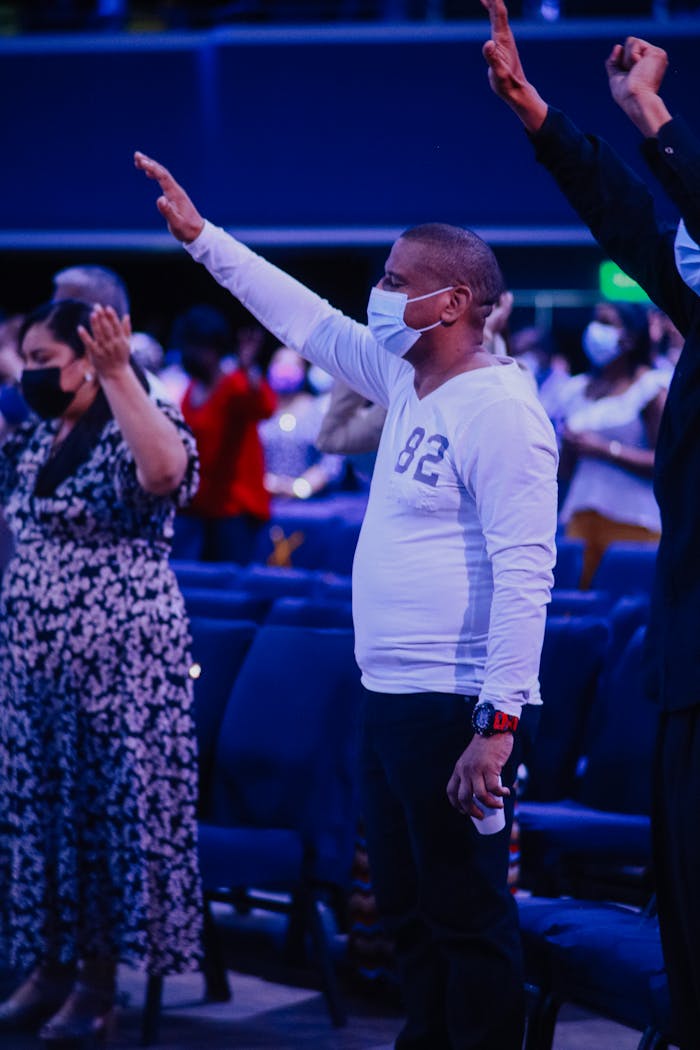 our-story A diverse group of adults wearing masks, praying at an indoor worship service.
